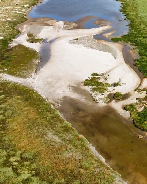 Vue aérienne de la grève à marée basse : une mare, du sable blanc et l’herbu
